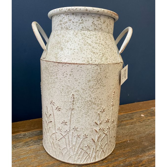 Decorative ceramic milk can with floral patterns on a wooden surface against a blue wall. Embossed Metal Milk Cans - Two Colours available at Quilted Cabin Home Decor.