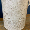 Textured ceramic vase with embossed designs on a wooden surface. Embossed Metal Milk Cans - Two Colours available at Quilted Cabin Home Decor.