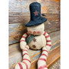 A burlap snowman with long limbs with red candy cane style stripes. It has a tall black hat and  a a green fabric scary. It is available at Quilted Cabin Home Decor.