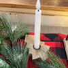 White candle in a wooden holder on a red and black checkered surface with greenery. Wooden Tree Taper Holder available at Quilted Cabin Home Decor.
