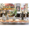 Decorative items including a vase with greenery, candle holders, and Christmas trees on a table in a store setting. Tarnished Santa Figurine available at Quilted Cabin Home Decor.