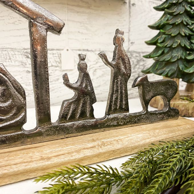 Decorative nativity scene with figures and a stable on a wooden base, surrounded by greenery. Nativity Silhouette available at Quilted Cabin Home Decor.