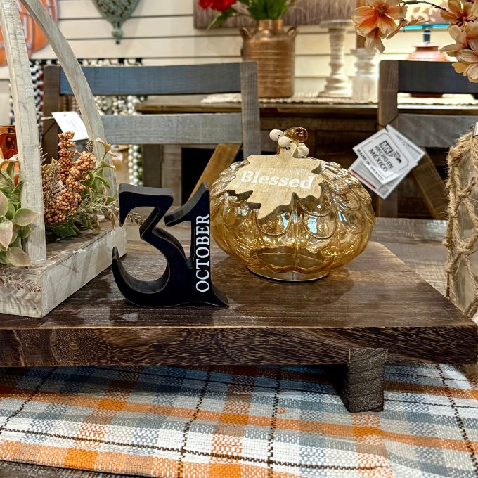 A decorative amber glass pumpkin with a leaf topper and a hanging 'Blessed' tag, displayed on a wooden table alongside a black number 3 and an October date marker in a rustic home decor setting. Available at Quilted Cabin in Airdrie
