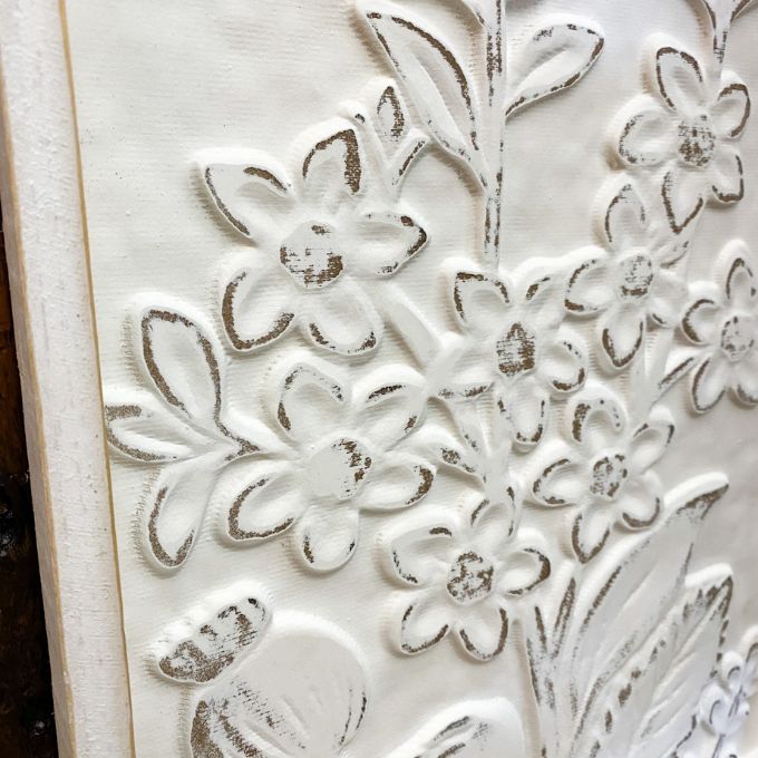 Close-up of a white embossed floral design on a textured surface. Embossed Whitewashed Flower Frame available at Quilted Cabin Home Decor.