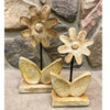 Decorative wooden flower sculptures on stands against a stone wall background. Wooden Daisies on Stand - Set of Two available at Quilted Cabin Home Decor.