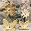 Decorative flower sculptures on stands against a stone wall. Wooden Daisies on Stand - Set of Two available at Quilted Cabin Home Decor.