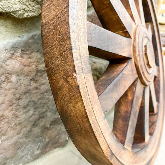 Close-up of a wooden wagon wheel against a stone wall background. Wooden Wagon Wheels - Two Sizes available at Quilted Cabin  Home Decor.