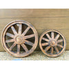 Two rustic wooden wheels against a wooden background. Wooden Wagon Wheels - Two Sizes available at Quilted Cabin  Home Decor.