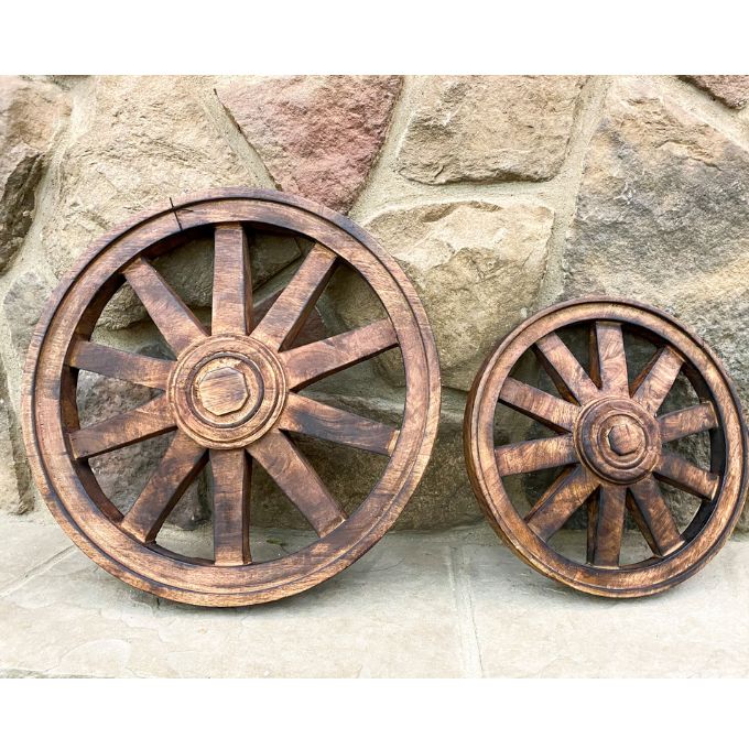 Two wooden wagon wheels against a stone wall background. Wooden Wagon Wheels - Two Sizes available at Quilted Cabin  Home Decor.