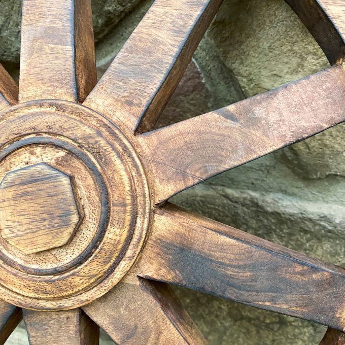 Close-up of a wooden wagon wheel against a stone wall background. Wooden Wagon Wheels - Two Sizes available at Quilted Cabin  Home Decor.
