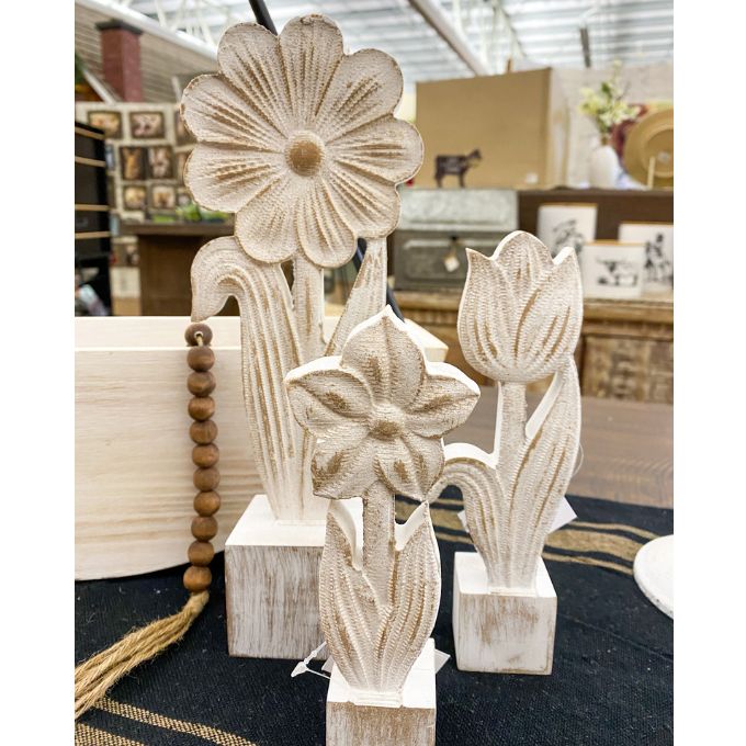 Decorative wooden flower sculptures on a dark surface with a blurred indoor background. Whitewashed Wooden Flowers - Three Styles available at Quilted Cabin Home Decor.