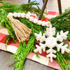 Distressed White Snowflake Hanger with Beaded Tassel is shown with a garland as part of a table display. Available at Quilted Cabin Home Decor.