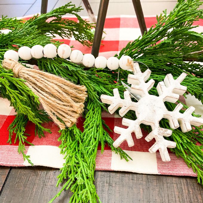 Distressed White Snowflake Hanger with Beaded Tassel is shown with a garland as part of a table display. Available at Quilted Cabin Home Decor.