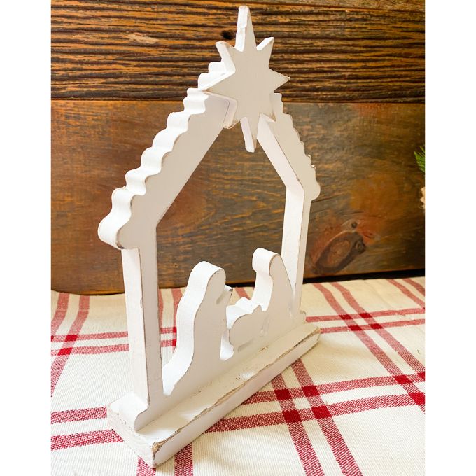 A farmhouse white distressed wooden cutout of the nativity scene under the Christmas star in the creche. The Distressed White Nativity cutout is a silhouette style nativity and available at Quilted Cabin Home Decor.