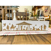 Decorative nativity scene box on a table with a plaid cloth in a home setting. Distressed White Carved Nativity Block Sign available at Quilted Cabin Home Decor.