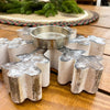 Decorative candle holder shaped like a snowflake on a wooden surface with a Christmas-themed background. Vintage Snowflake Tea Light Holder available at Quilted Cabin Home Decor.