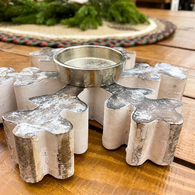 Decorative candle holder shaped like a snowflake on a wooden surface with a Christmas-themed background. Vintage Snowflake Tea Light Holder available at Quilted Cabin Home Decor.