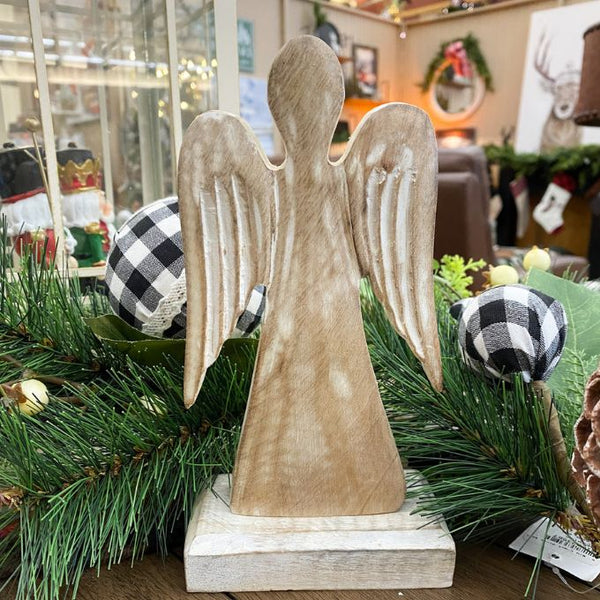 Wooden angel figurine on a base with Christmas decorations in the background. Distressed White Wooden Angel available at Quilted Cabin Home Decor.
