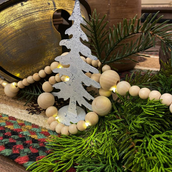 A light wood beaded garland with lights throughout is shown as part of Christmas decor. Available at Quilted Cabin Home Decor.