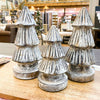 Three decorative Christmas tree figurines on a wooden surface with a blurred indoor setting in the background. Distressed Carved Trees - Two Sizes available at Quilted Cabin Home 