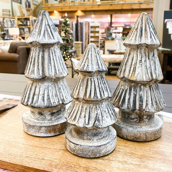 Three decorative Christmas tree figurines on a wooden surface with a blurred indoor setting in the background. Distressed Carved Trees - Two Sizes available at Quilted Cabin Home 