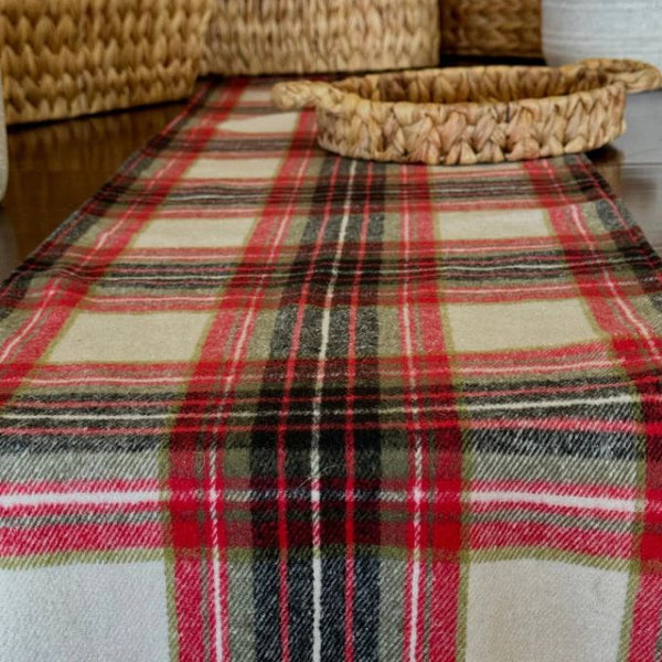 Plaid table runner on a table with a woven basket. Noel Plaid 72" Table Runner is available at Quilted Cabin Home Decor.