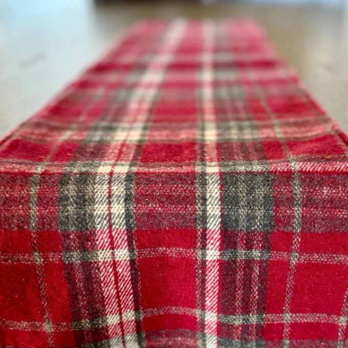 Red plaid table runner with a   on a flat surface. Merry Plaid 48" Table Runner available at Quilted Cabin Home Decor.