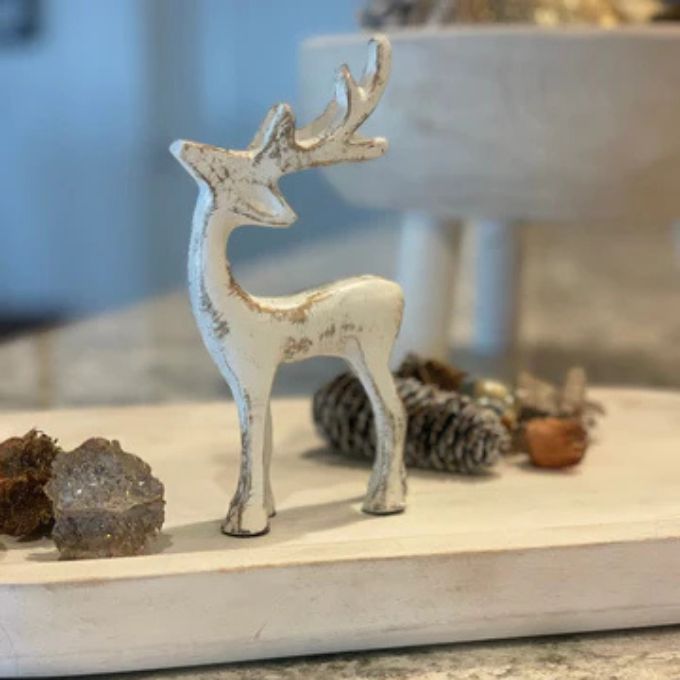 Decorative white deer figurine on a surface with blurred background. Aluminum reindeer available at Quilted Cabin Home Decor.