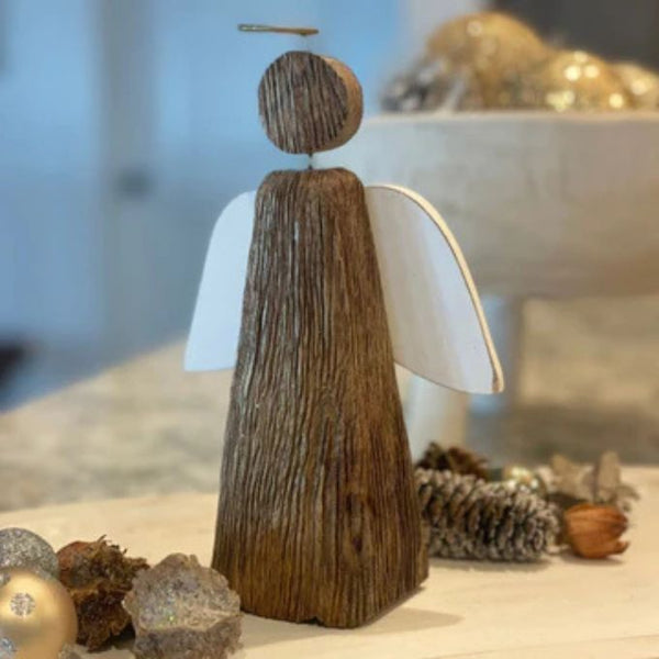 Wooden angel figurine with white wings on a surface with decorative items. Grooved Wood Angel Figurine available at Quilted Cabin Home Decor.