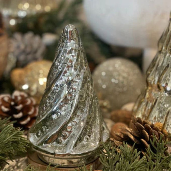 Decorative glass tree with pinecones and greenery on a blurred festive background. Silver Swirl Mercury Glass Tree available at Quilted Cabin Home Decor.