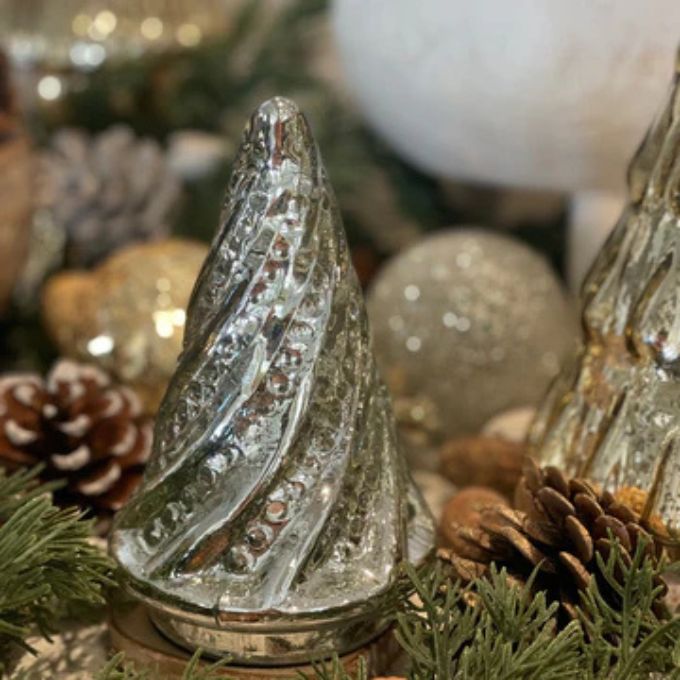 Decorative glass tree with pinecones and greenery on a blurred festive background. Silver Swirl Mercury Glass Tree available at Quilted Cabin Home Decor.