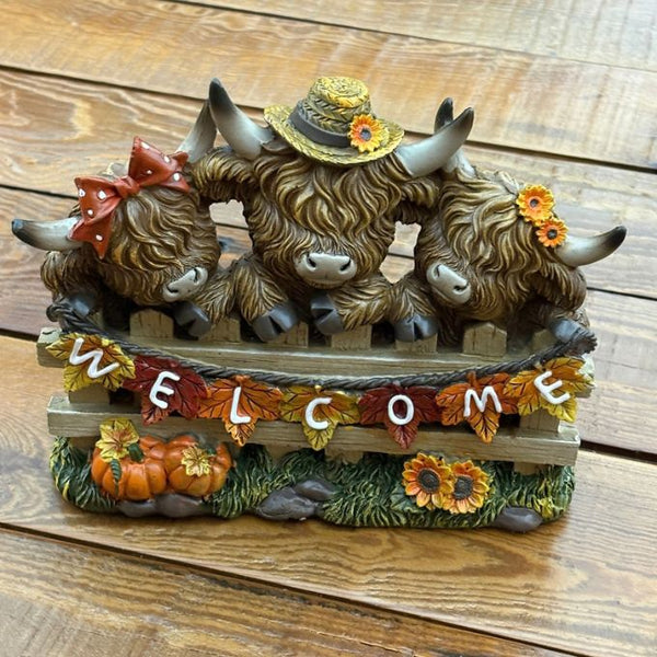three  highland cows behind a welcome fence with sunflowers and pumpkins available at Quilted Cabin in Airdrie