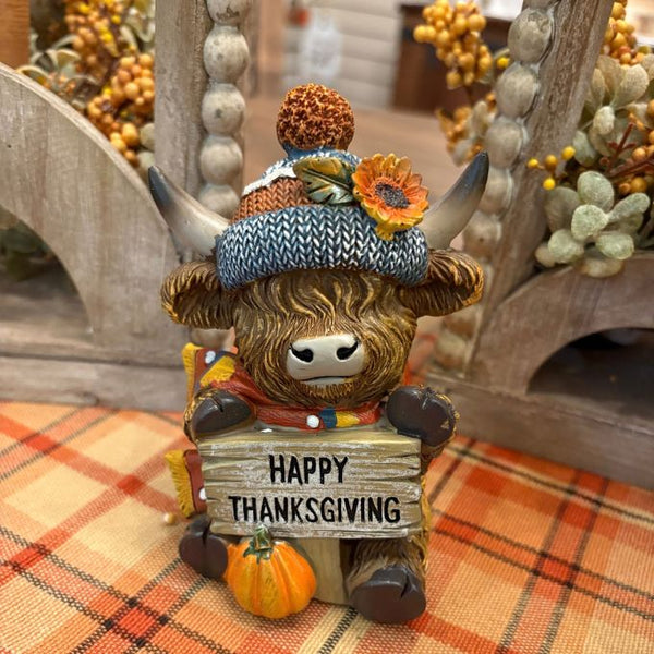 Highland cow with blue cap holding a Happy Thanksgiving sign available at Quilted Cabin in Airdrie