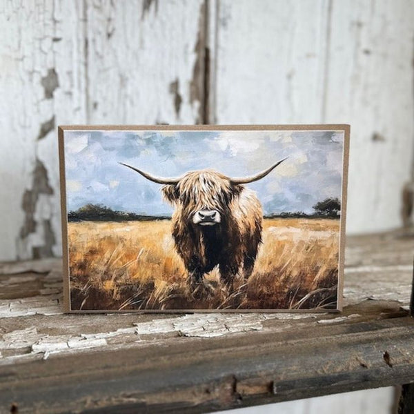 Wooden block art print of a highland cow in a field with a rustic wooden background. Grazing Highland Block Art available at Quilted Cabin Home Decor.