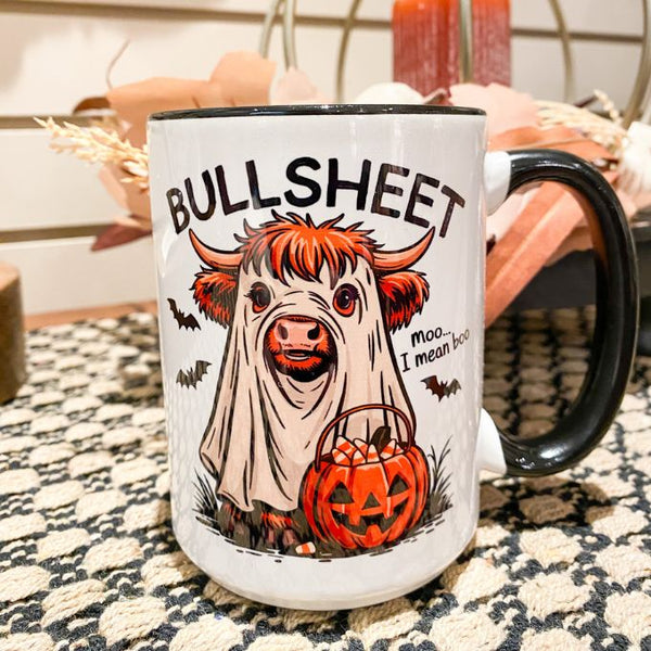 Mug with a ghostly cow holding a pumpkin and 'BULLSHEET mo... I mean boo!' text. The Bullsheet Highland Cow Halloween Mug is available at Quilted Cabin Home Decor.