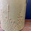 Ceramic vase with floral embossing on a wooden surface. Embossed Metal Milk Cans - Two Colours available at Quilted Cabin Home Decor.