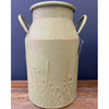 Green ceramic milk can with floral patterns on a wooden surface against a blue background. Embossed Metal Milk Cans - Two Colours available at Quilted Cabin Home Decor.