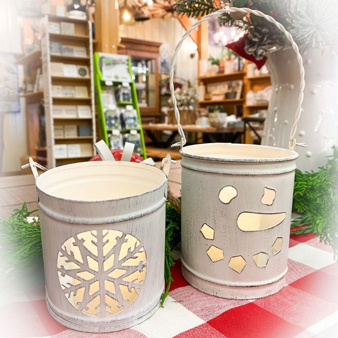 Two white tin lanterns, one with a cut out snowman face and the other with a snowflake. Available at Quilted Cabin Home Decor.