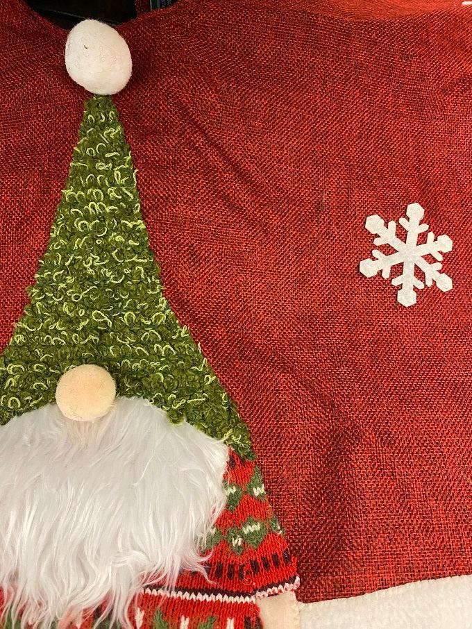 The Kringle Gnome tree skirt in red is shown. It has a festive gnome appliqued on it along with snowflakes. It is trimmed in faux fur.