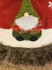 The Kringle Gnome tree skirt in red is shown. It has a festive gnome appliqued on it along with snowflakes. It is trimmed in faux fur.