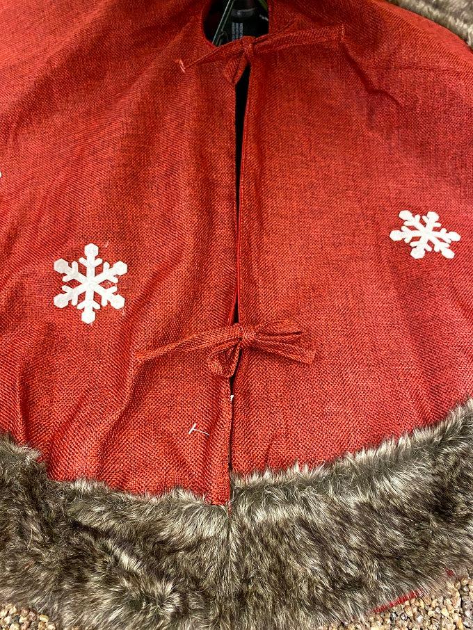 The Kringle Gnome tree skirt in red is shown. It has a festive gnome appliqued on it along with snowflakes. It is trimmed in faux fur.