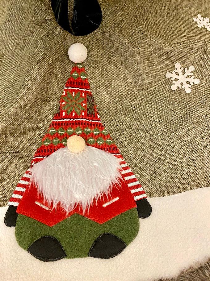 The Kringle Gnome tree skirt in green is shown. It has a festive gnome appliqued on it along with snowflakes. It is trimmed in faux fur.