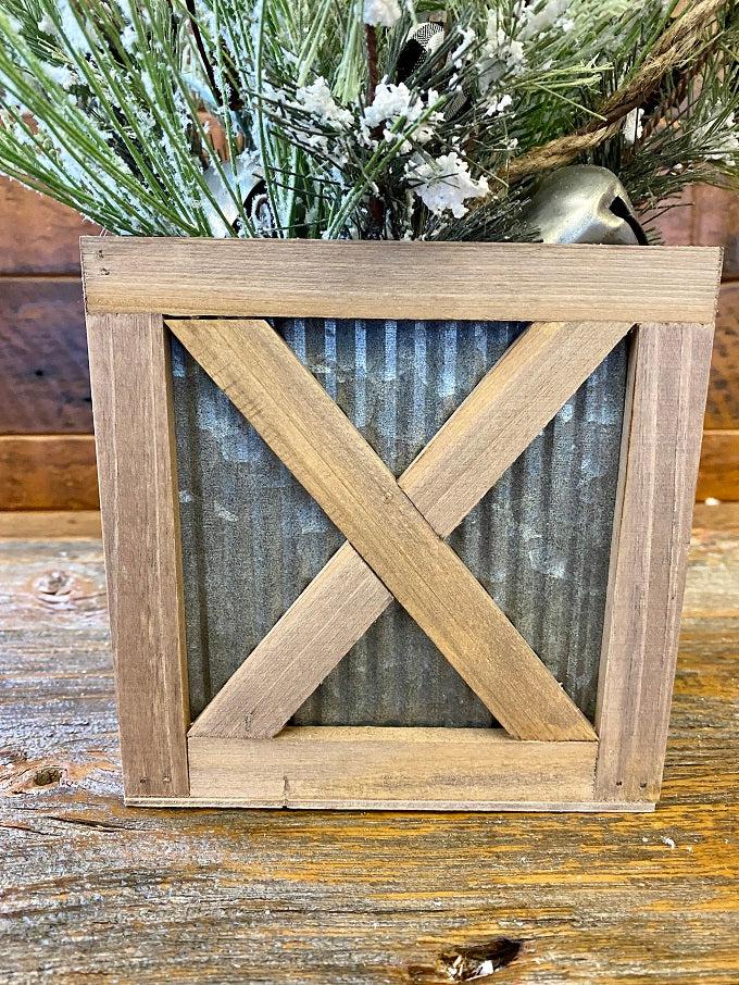   Wood trimmed galvanized corrugated metal boxes in two sizes are filled with floral. The boxes have an wood strapping on the outside in the shape of an X and all of the edges are faced with wood. 