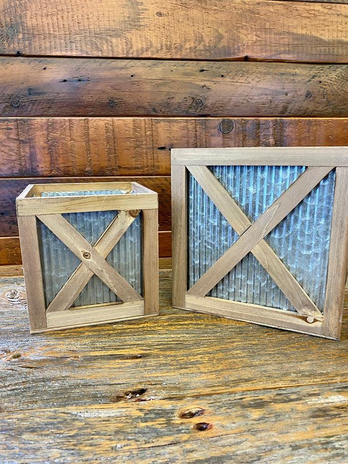   Wood trimmed galvanized corrugated metal boxes in two sizes are filled with floral. The boxes have an wood strapping on the outside in the shape of an X and all of the edges are faced with wood. 