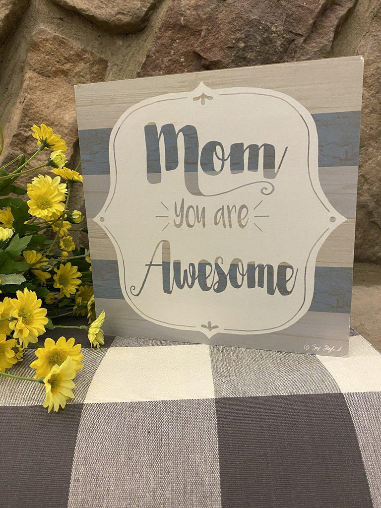 A lightweight box sign that says Mom you are awesome in the centre. It can be hung or sit on a shelf. The background of the sign is painted in grey and blue stripes. The stripes are visible through the lettering on the front. 