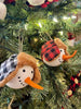 Two Holiday snowmen ornaments are shown. These ornaments are the head of the snowman with eyes made to look like coal and a carrot-like nose. One has a black and white plaid hat and the other has a red and black plaid hat.