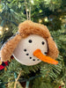 The Black and White Holiday Snowman Ornament is the head of a snowman with a black and white cap with fuzzy ear flaps.  He has two eyes made to look like coal and a carrot-like nose.