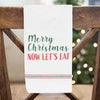 A white farmhouse Christmas dish towel that says Merry Christmas now let's eat.