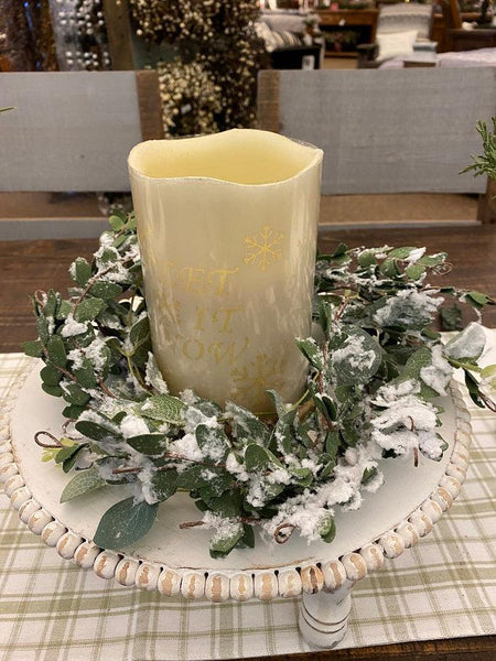 A succulent wreath that is flocked to look like snow has just fallen. It is green and made of different kinds of succulents. It is shown here with a candle. 