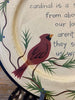 A close up of a round wooden plate showing a red cardinal on a cream coloured painted background and features the text:  A beautiful red cardinal is a sign from above that our loved ones aren't far...they surround us with love.